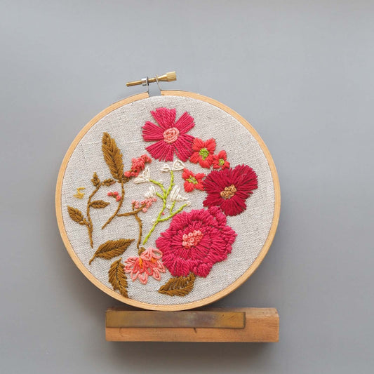 Red and burgundy floral pattern stitched on to a 5 inch embroidery hoop against a gray background
