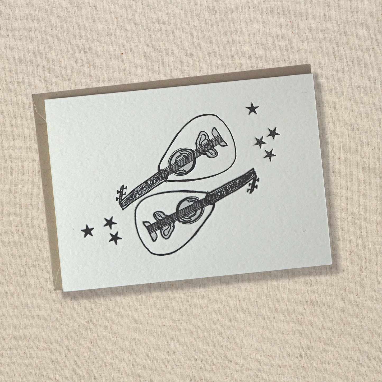 notecard with two out instruments with seven stars letterpress printed in black in on light cotton paper on top of a light kraft envelope.