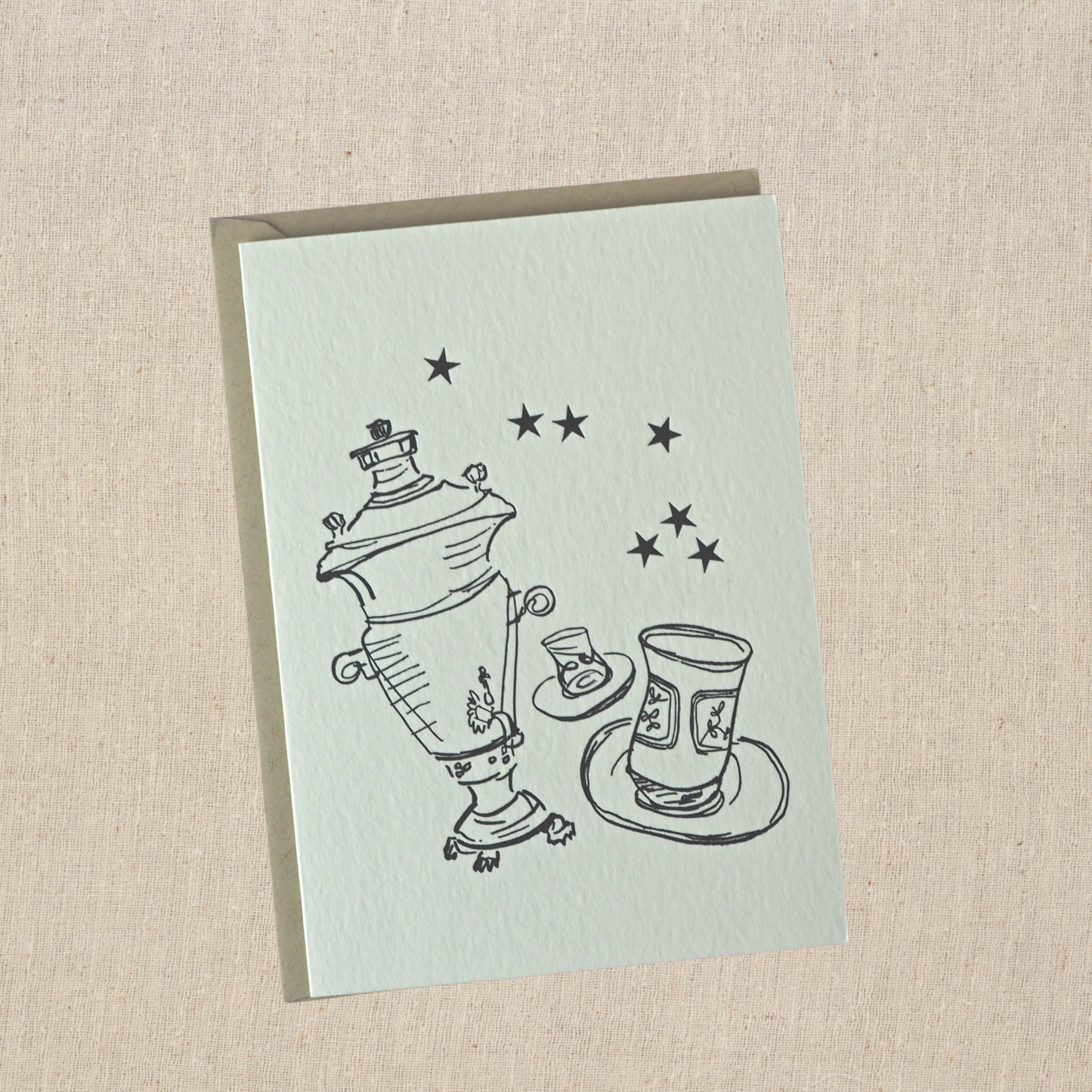 Greeting card with samovar , two tea glasses, and 7 stars letterpress printed in black ink on natural cotton paper on top of a light kraft envelope