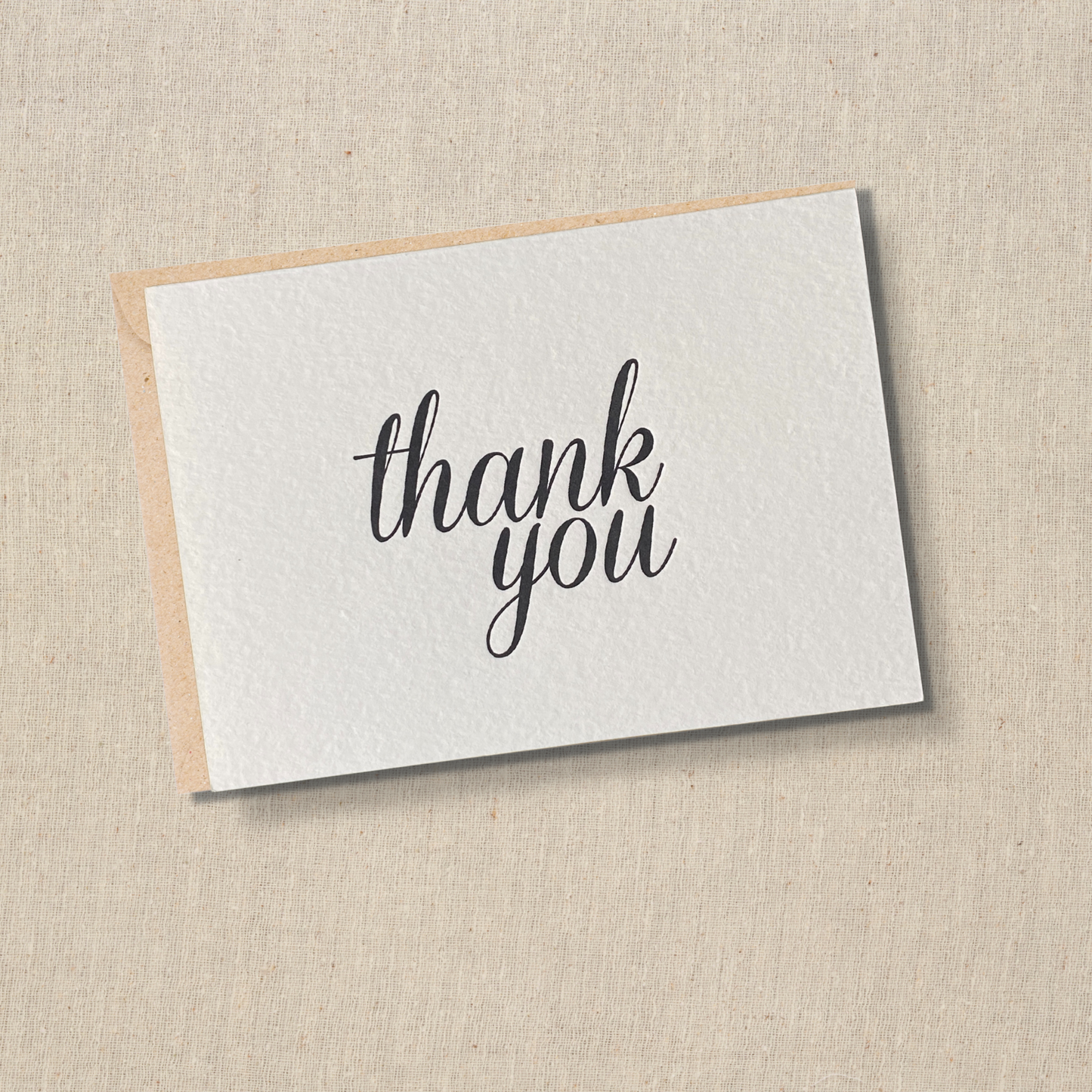 Notecard with black ink that says thank you in modern script. Kraft envelop is below card.