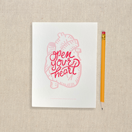 5 x 7 letterpress print with pink anatomical heart one drawing and red lettering that says open your heart