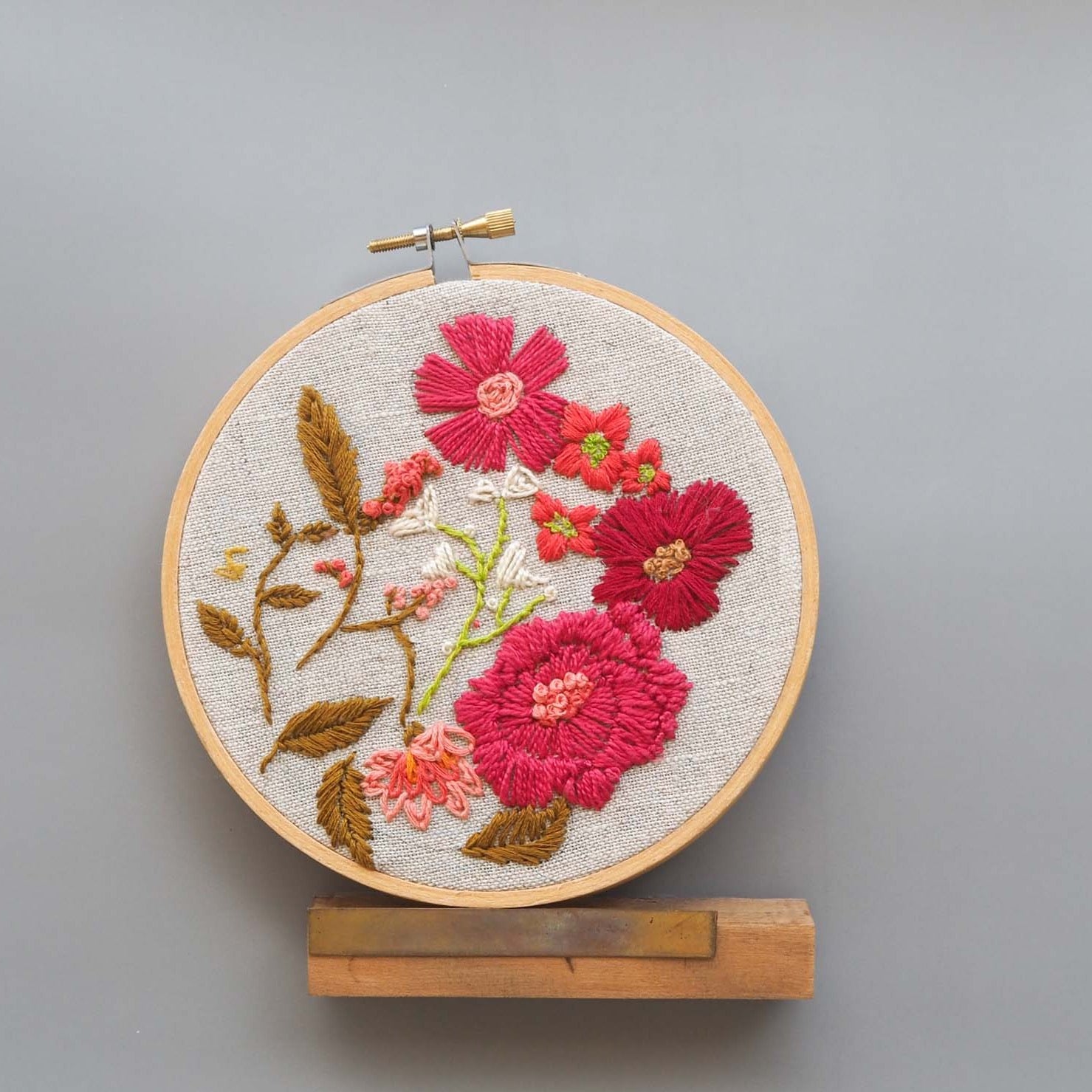 Red and burgundy floral pattern stitched on to a 5 inch embroidery hoop against a gray background 