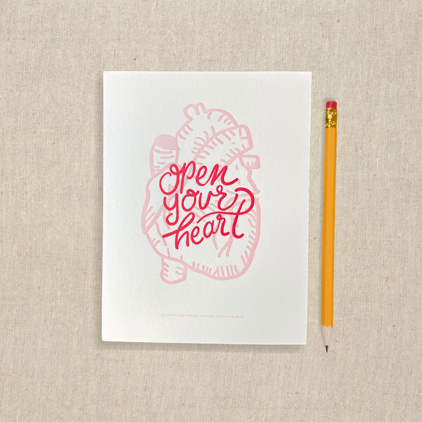 5 x 7 letterpress print with pink anatomical heart one drawing and red lettering that says open your heart 